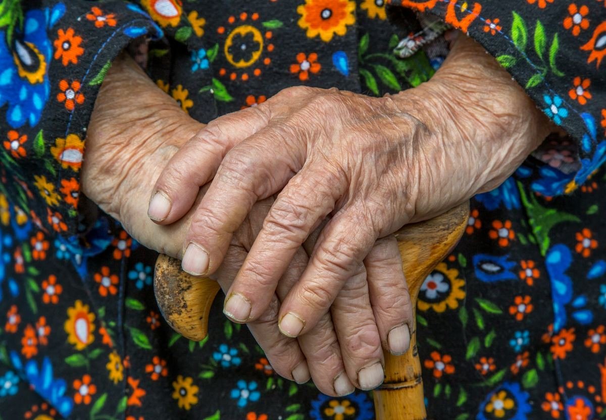 An older person’s hands resting on a walking stick.