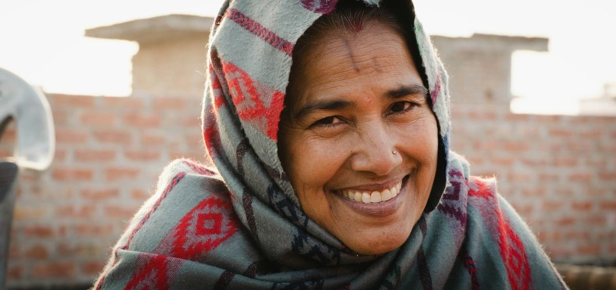 A smiling woman wrapped in a red and grey shawl.