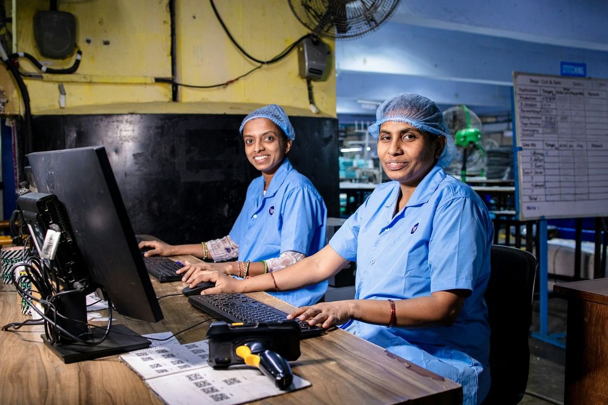 Two healthcare workers in blue scrubs smiling at a computer workstation.