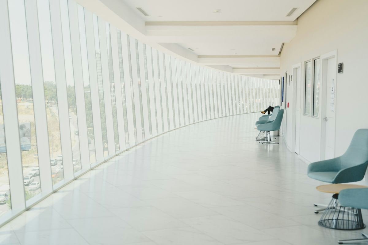 A bright curved corridor with tall windows and lounge chairs.