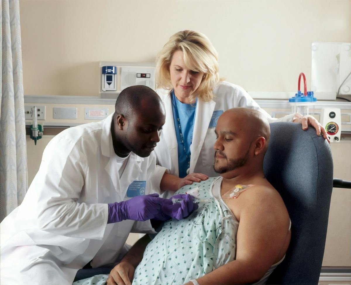 A clinician administering treatment through a chest port while a nurse supports the patient.